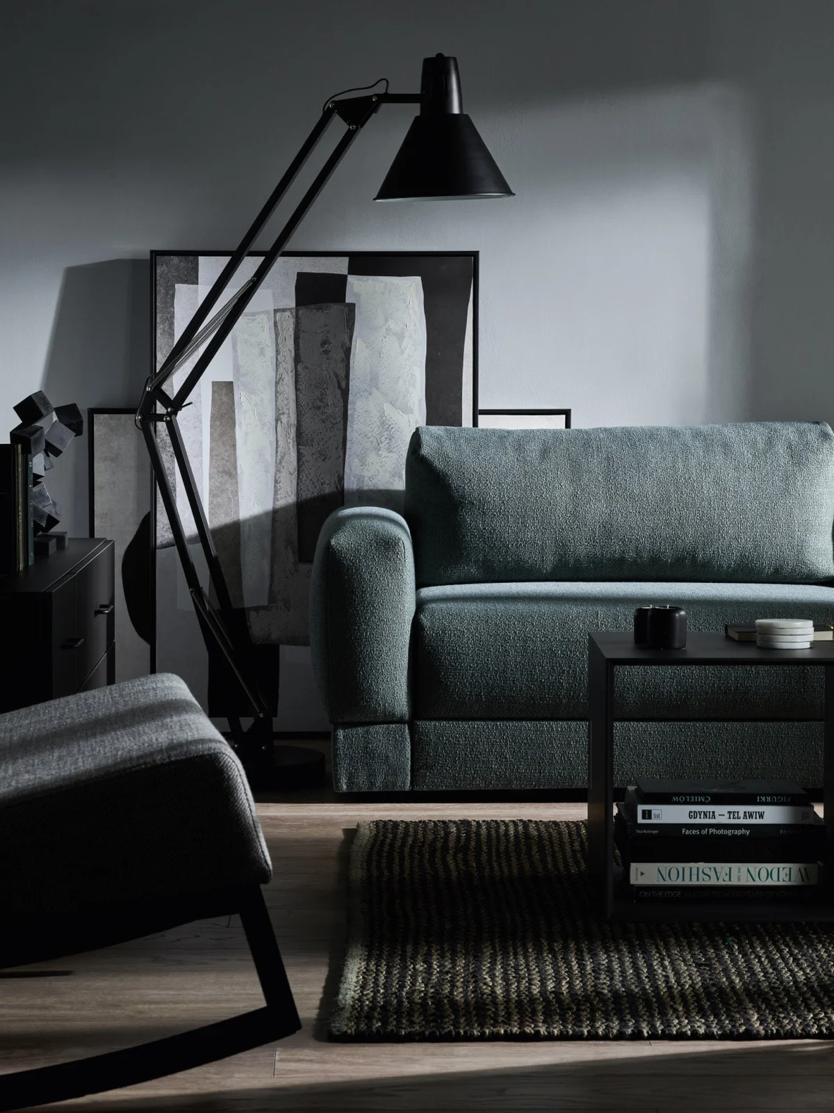 Ciemnoszara sofa i czarna lampa podłogowa na tle szarej ściany